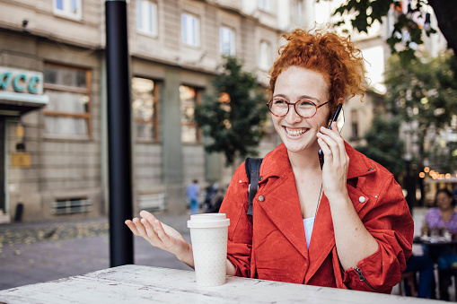 Portrait of a beautiful young woman sitting at the cafe, talking on mobile phone and enjoying coffee.