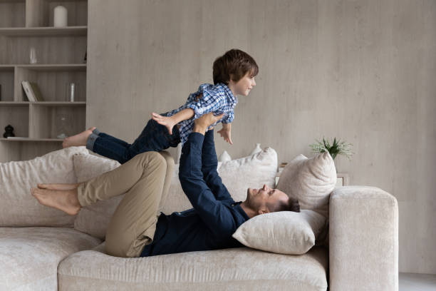 istock Dad lying on couch lifts on outstretched hands little son 1384369469