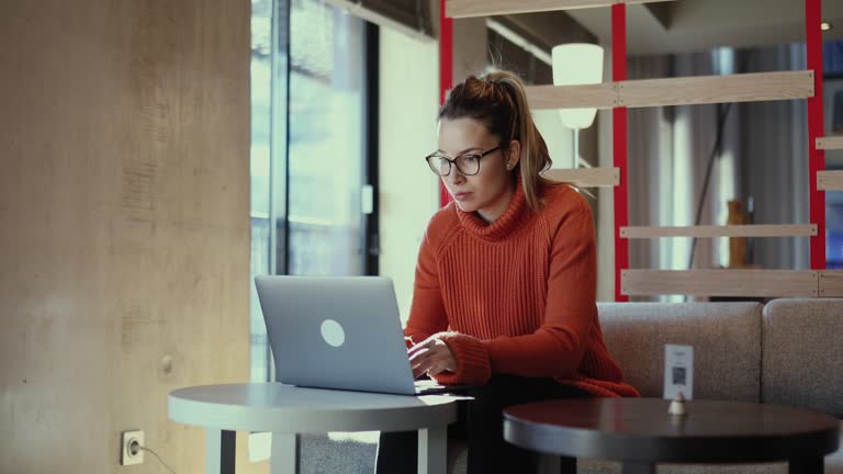 The woman sits at the table and uses a laptop to correspond with her colleagues.
