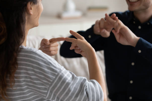 Couple communicating at home using sign language, closeup Young positive couple sit on sofa at home communicating using sign language, friends talking indoor showing fingers gestures, having fun, leading pleasant conversation, people with disability concept signing stock pictures, royalty-free photos & images