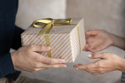 Holiday celebration, family life event, anniversary, make surprise concept. Close up male hands giving long-awaited gift to sweetheart wife, congrats her on birthday, enjoy moment of receiving giftbox
