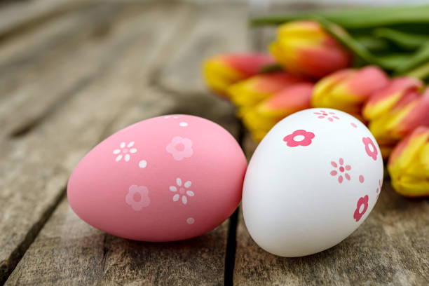 Two Easter eggs and a bouquet of tulips on a rustic wooden table. Selective focus.