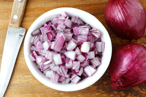 chopped raw red onion in white ceramic bowl over rustic wooden table. Close up view