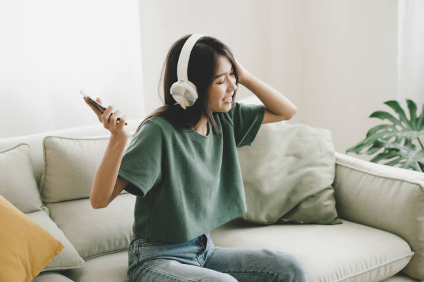 joven asiática sentada en el sofá. ella escuchando música y bailando en la sala de estar. ella feliz y relajante en el tiempo libre los fines de semana - fun time audio fotografías e imágenes de stock