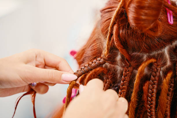 istock Hairdresser's hands braid girl's ginger dreadlocks. 1384411507