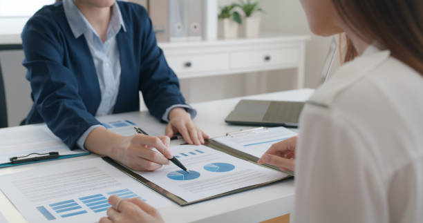 Asia stock trader agent or Sale tax loan broker advice brief and point hand to graph report talk to client at office desk show budget chart data or legal result on claim form. Trust will in work plan. agente de comercio de acciones de asia o corredor de préstamos fiscales de venta breve y punto a gráfico informe hable con el cliente en el escritorio de la oficina muestre los datos del gráfico de presupuesto o el resultado legal en el formulario de re