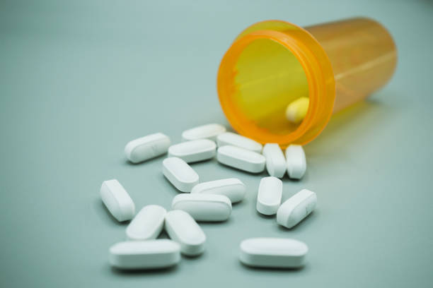 Prescription bottle with large white pills spilling out. Gray background.