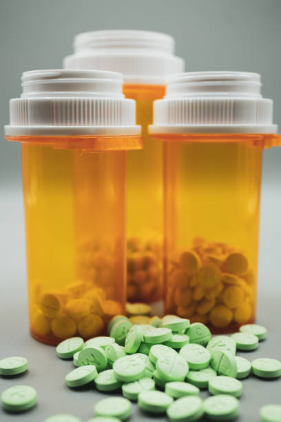 Close-up of three prescription bottles of various sizes with green pills scattered in foreground. Gray background