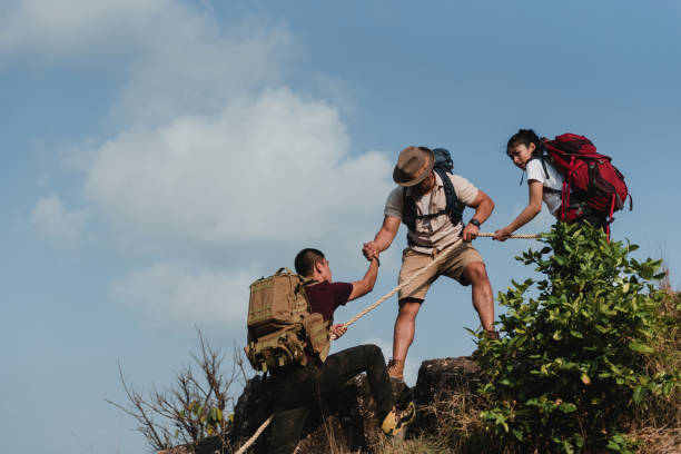 trois adolescents asiatiques, alpiniste, randonneur et voyageur. voyager au sommet d’une montagne, sous le soleil, donner un coup de main, aider les autres et tirer vers le haut, aider et travailler en équipe concept. - rescue mountain horizontal three people photos et images de collection