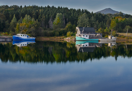 Colorful boats and green forest comprise a quiet waterside scene along a less-traveled road in Nova Scotia.