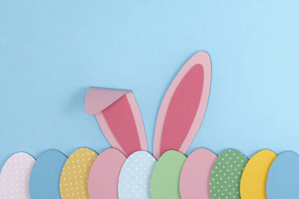 istock Pink Bunny rabbit ears and painted Easter eggs cutting out paper on blue background. 1384434740