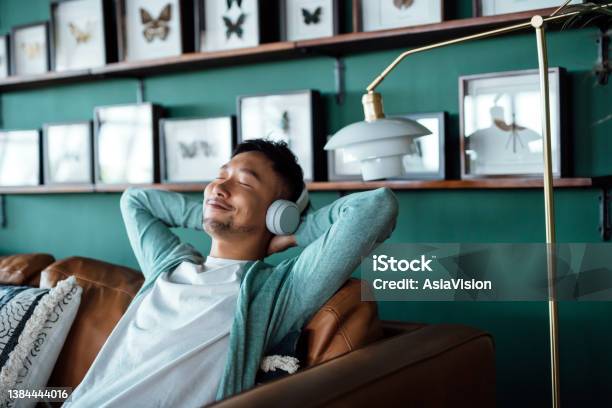 Young Asian Man With Hands Behind Head Relaxing On Sofa And Listening To Music With Headphones At Home Relaxed Young Man Lying On Sofa With Music Relaxing Lifestyle People And Technology Concept Stock Photo - Download Image Now
