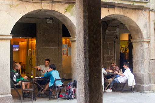Santiago de Compostela, Spain- July 9, 2021: Street stone arches and columns, sidewalk cafes, people sitting down in old town Santiago de Compostela in summertime, street view, A Coruna province, Galicia, Spain.
