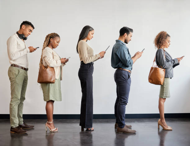 近代的なオフィスで並んで待っている若いビジネスマンのグループがスマートフォンを使用しているショット - 行列 ストックフォトと画像