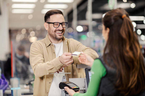 a happy man giving credit card to cashier in supermarket and paying check. - store retail supermarket checkout counter imagens e fotografias de stock