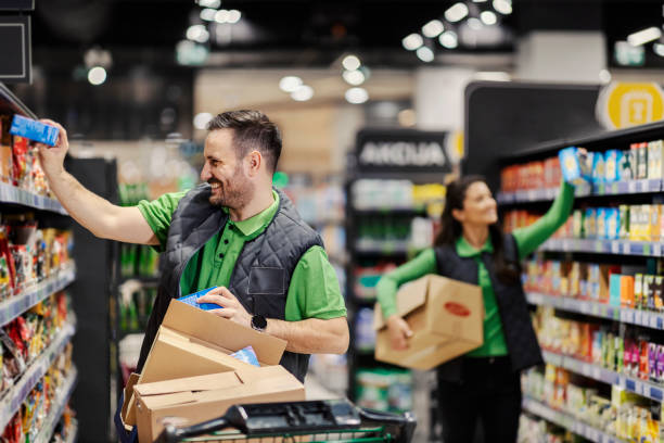 The employees putting groceries on aisle and exposing them at supermarket. stock photo