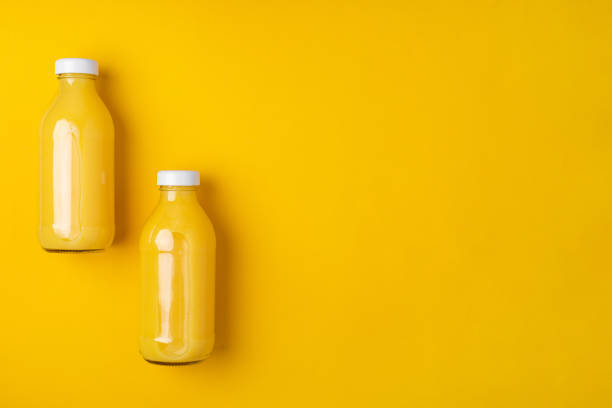istock Two glass bottles with orange juice on a bright yellow background 1384454974