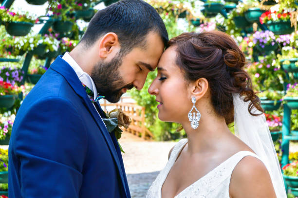 Tender moment of a newlywed LGBTQ couple embracing beside a vibrant pink wall with floral greenery, expressing love, affection and the optimism of their shared future.