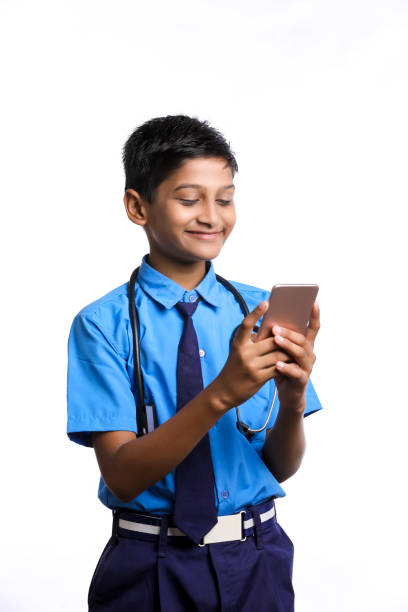 indyjski chłopiec w mundurku szkolnym ze stetoskopem i za pomocą smartfona na białym tle. - technology typing male beauty asian and indian ethnicities zdjęcia i obrazy z banku zdj�ęć