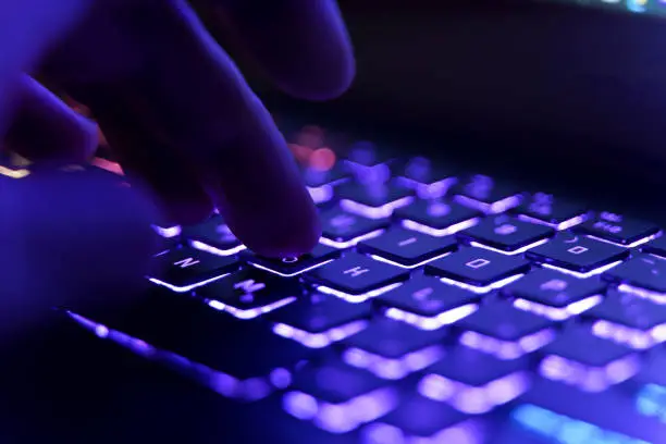 Photo of Working on a neon computer keyboard with colored backlighting. Computer video games, hacking, technology, internet concept. Selected focus.