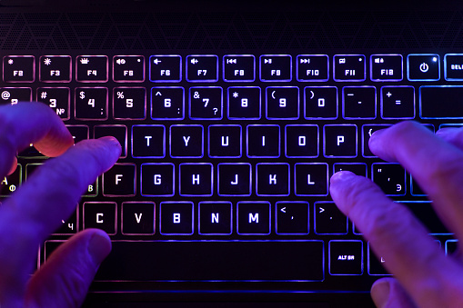 Working on a neon computer keyboard with colored backlighting. Computer video games, hacking, technology, internet concept. Selected focus. High quality photo