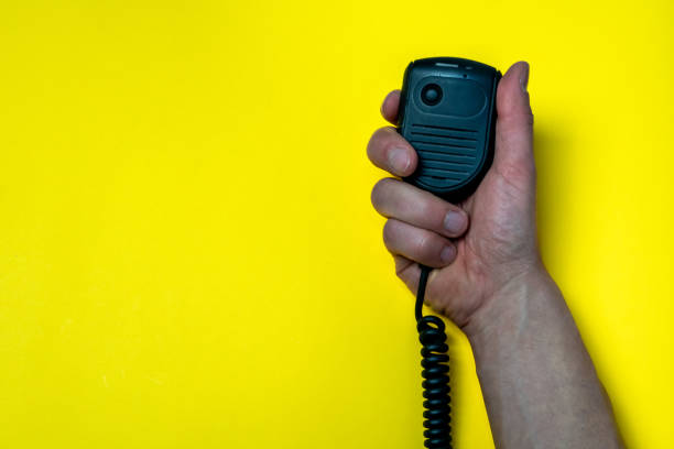istock Hand holding black broadcast microphone on yellow background with side space. 1384468150