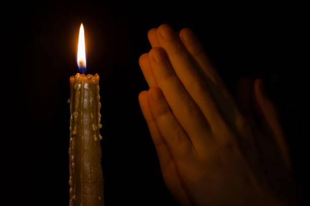 istock Burning candle and praying hands on black background. 1384470555