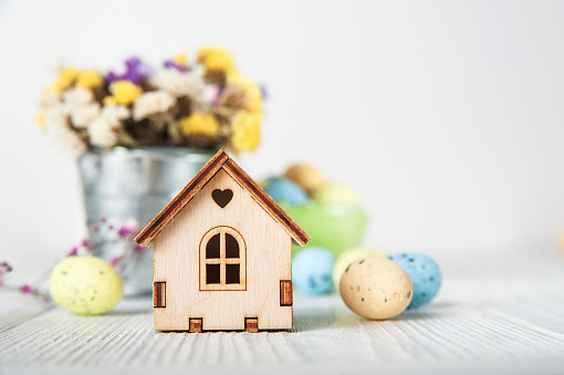 Happy Easter greeting card. Miniature wooden house.Rabbits, colorful eggs, spring flowers with tag for text.