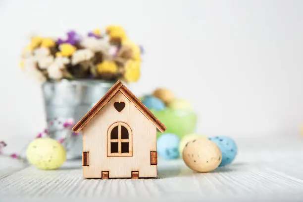 Photo of Happy Easter greeting card. Miniature wooden house. Rabbits, colorful eggs, spring flowers with tag for text..