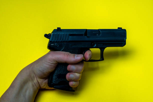 istock Hand holding black handgun on yellow background. 1384472977