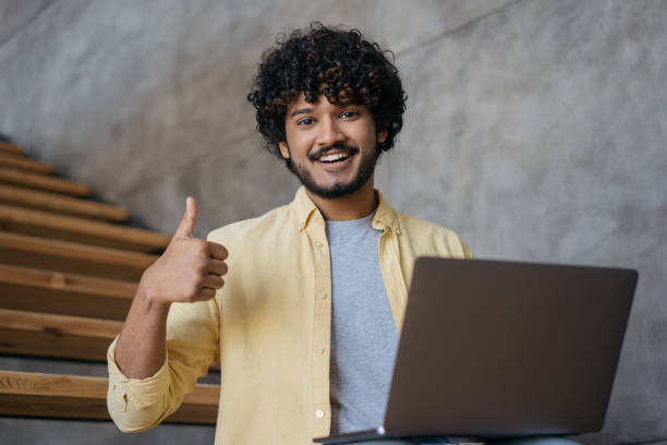 istock Indian  freelancer using laptop computer showing thumb up looking at camera working online from home. Asian student studying, watching training courses, online education concept 1384475240