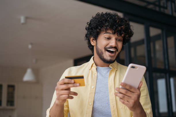 indischer mann mit kreditkarte mit handy-shopping online. glückliche freelancer erhalten zahlung, überprüfen sie das kartenguthaben. emotionaler typ, der online-essen bestellt und auf den digitalen bildschirm schaut - asian ethnicity surprise men shock stock-fotos und bilder