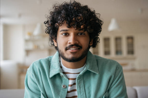 étudiant indien souriant écoutant la leçon en ligne assis à la maison. bel homme asiatique ayant un appel vidéo, une communication en ligne. concept de vidéoconférence - indian ethnicity audio photos et images de collection