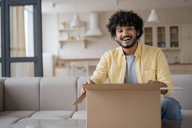 istock Indian man unpacking box looking at camera sitting at home, copy space. Unpacking parcel, delivery concept 1384477381