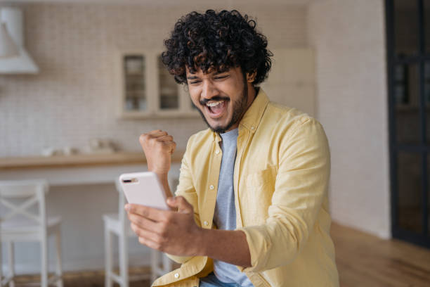 istock Indian man using smart phone playing mobile game. Young excited asian gambler holding mobile phone win money celebration success, sport betting concept. Emotional freelancer receive payment 1384479211