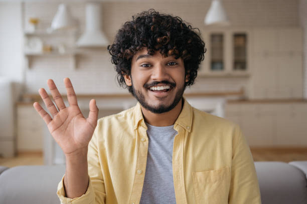 istock Smiling Indian man freelancer having video call working online from home. Young happy influencer recording video waving hand talking to camera 1384481968