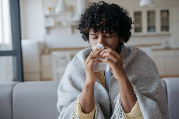 Sick Indian man with runny nose holding paper napkins near face sitting at home. Flu, virus, allergy concept stock photo