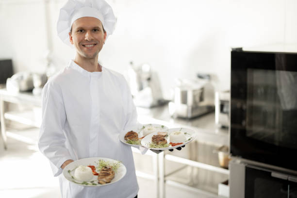 istock Smiling chef in uniform standing with ready meals in the kitchen 1384494526