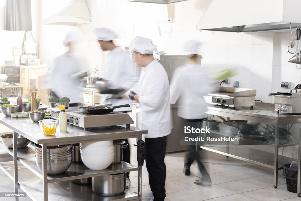 Chef cooks working in professional kitchen Chef cooks working in professional kitchen. Chefs hurry up, actively cooking meals for restaurant. Long exposure with motion blurred figures Kitchen Stock Photo