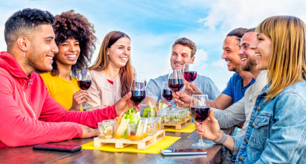 young adult group of friends having a glass of wine on a rooftop bar restaurant outdoors. people enjoying happy hour together drinking alcohol and eating sitting on a table. fun and lifestyle concept young adult group of friends having a glass of wine on a rooftop bar restaurant outdoors. people enjoying happy hour together drinking alcohol and eating sitting on a table. fun and lifestyle concept big family sunset stock pictures, royalty-free photos & images