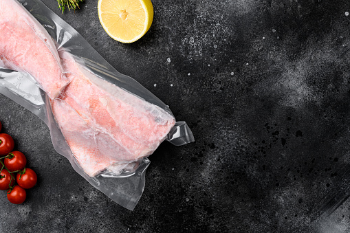 Orange roughy frozen pack fish meat set, with herbs, on black dark stone table background, top view flat lay, with copy space for text