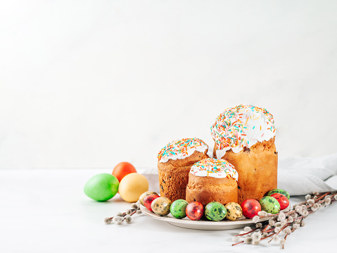 Traditional Russian Ukrainian Easter Cake Kulich. Orthodox Christian Easter Bread or Easter Cake with frosting, Easter Eggs and willow twigs on white marble background. Copy space for text or design