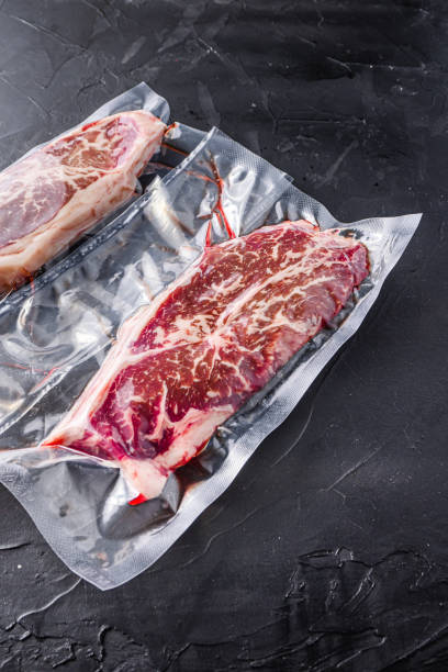 istock Top blade steak,  vacuum packed organic beef for sous vide cooking  on black textured background, top view. 1384517634