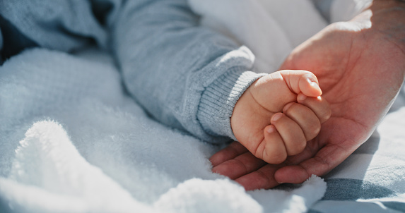 hand of a father holding the small hand of his newborn daughter in the maternity hospital. family concept, baby care and maternal and paternal love