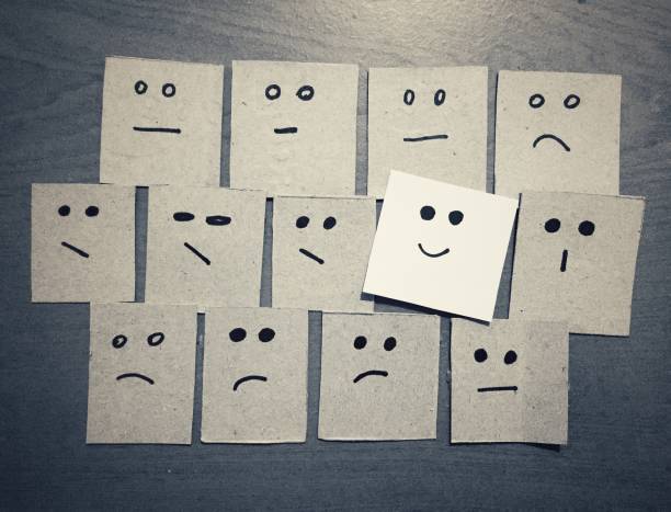 istock Concept for a positive attitude with small office notes with multiple faces (bad emogi) and of that stands out with smile (smile emogi). 1384524345
