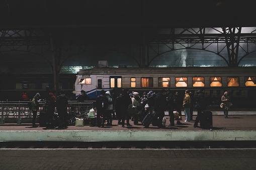 Lviv, Ukraine - March 4, 2022: People with luggage stand on a train station platform at night in Lviv, Ukraine