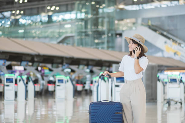 istock Young woman using smartphone and  hand holding luggage handle before checking flight time in airport, Transport, insurance, travel and vacation concepts 1384533395
