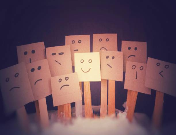 A concept for a positive attitude with a small note on a mini wooden stick with many faces (bad emoji) and one that stands out with a smile (smile emoji).
