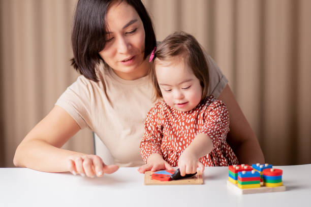 cute baby girl with down syndrome learning with educational toys at home with mom,child special education in the family stock photo