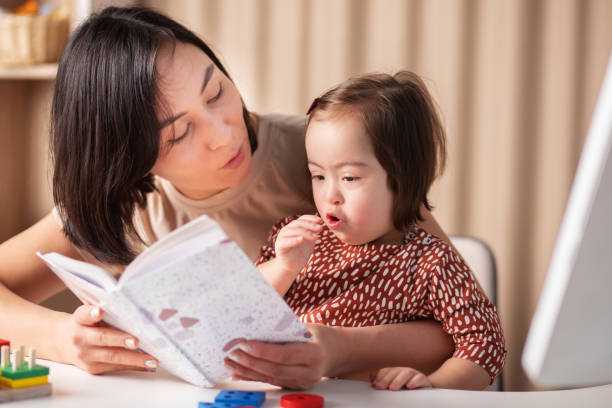 training and education of children with down syndrome, a girl with her mother and a book at home read a textbook stock photo
